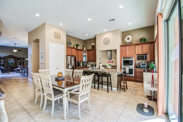 tiled dining room featuring ceiling fan, sink, and a towering ceiling