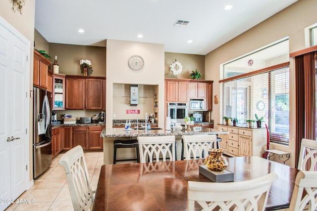 kitchen featuring light tile patterned floors, a breakfast bar, stainless steel appliances, light stone countertops, and an island with sink