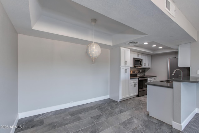 kitchen with pendant lighting, white cabinets, stainless steel appliances, sink, and a tray ceiling