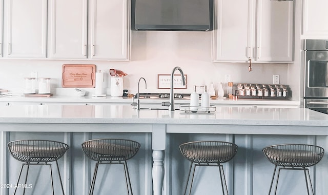 kitchen with sink, double wall oven, light stone counters, white cabinetry, and a breakfast bar area