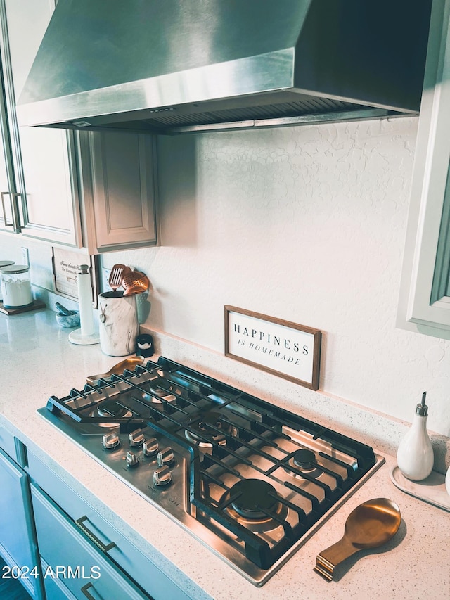 interior details featuring wall chimney exhaust hood, blue cabinets, and stainless steel gas cooktop