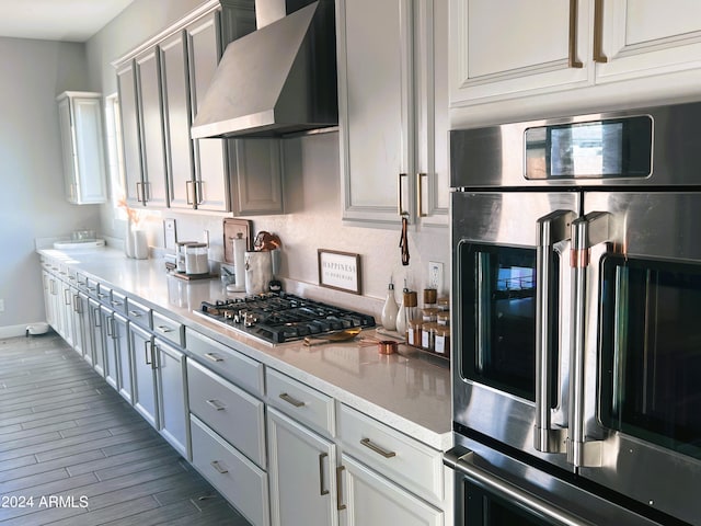 kitchen with hardwood / wood-style flooring, wall chimney range hood, and appliances with stainless steel finishes