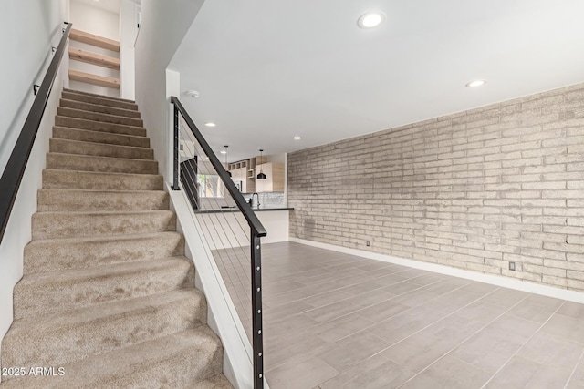 staircase with brick wall, recessed lighting, and baseboards