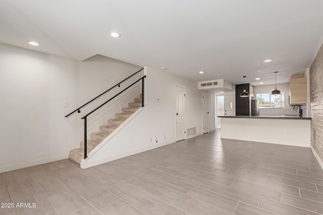 unfurnished living room with a sink, recessed lighting, stairs, and baseboards