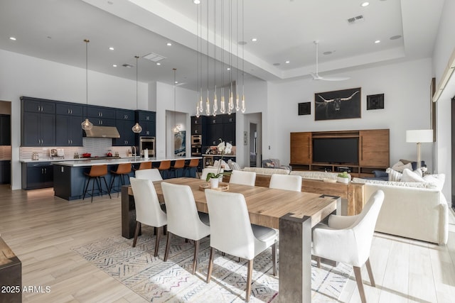 dining space with a high ceiling, light wood-type flooring, a tray ceiling, and ceiling fan