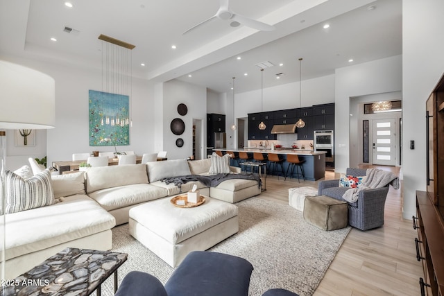 living room featuring ceiling fan, light hardwood / wood-style floors, and a towering ceiling