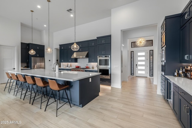 kitchen with a kitchen island with sink, tasteful backsplash, decorative light fixtures, a kitchen bar, and stainless steel appliances