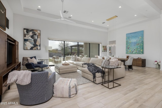 living room with ceiling fan, a raised ceiling, light wood-type flooring, and a towering ceiling