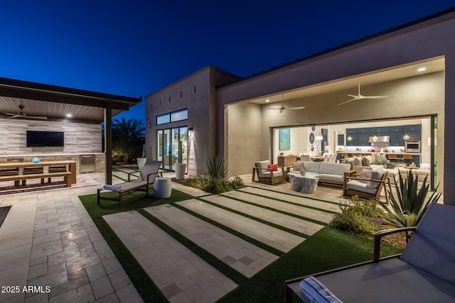 patio at night featuring ceiling fan, an outdoor living space, and exterior kitchen