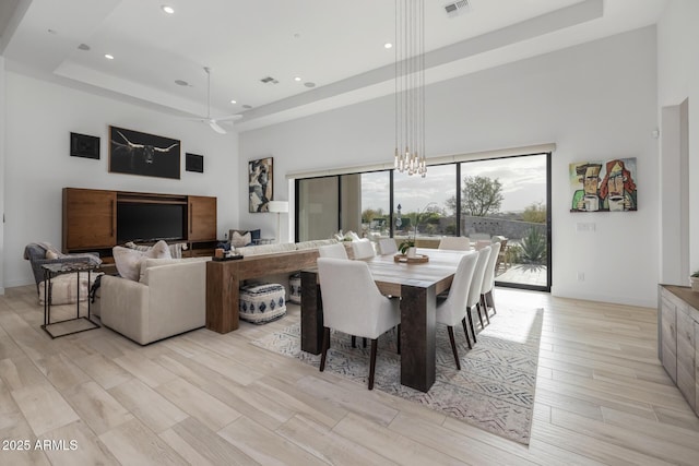 dining room featuring a high ceiling, light wood-type flooring, a raised ceiling, and ceiling fan