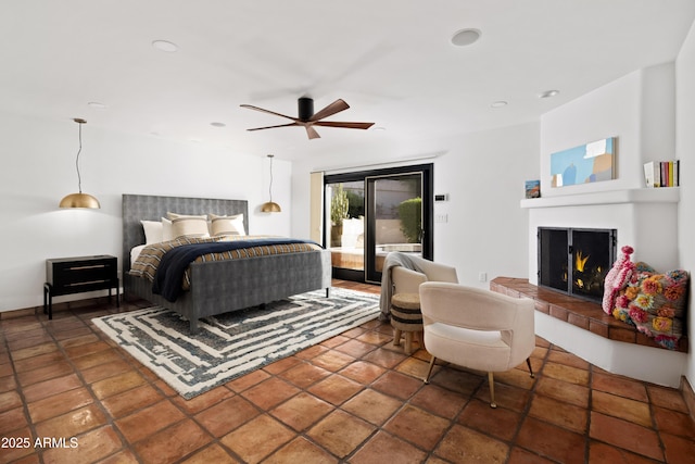 bedroom with access to outside, a tiled fireplace, ceiling fan, and dark tile patterned floors