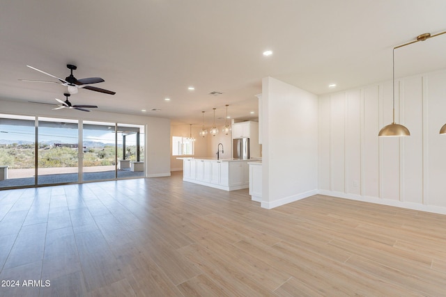 unfurnished living room featuring light wood-type flooring, ceiling fan, and sink