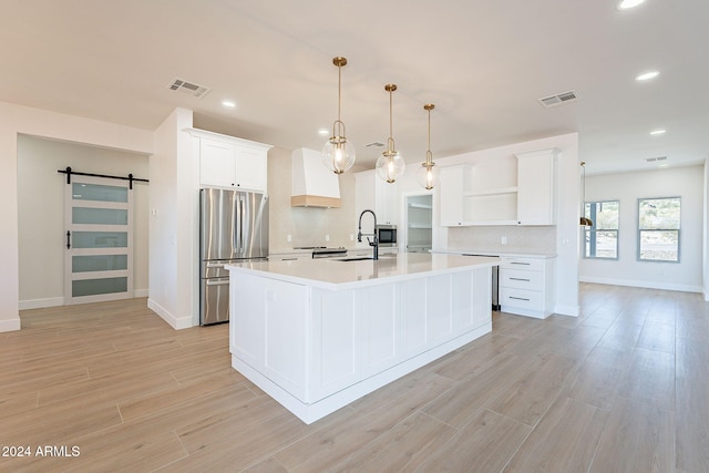 kitchen featuring stainless steel fridge, light wood-type flooring, a kitchen island with sink, a barn door, and hanging light fixtures