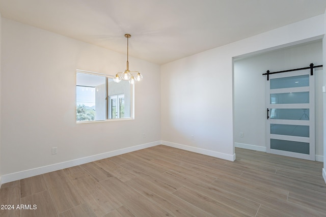 empty room featuring a barn door, a notable chandelier, and light wood-type flooring