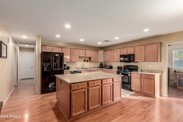 kitchen with sink, a center island, light stone counters, black appliances, and light wood-type flooring