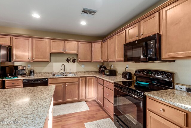 kitchen with light stone countertops, sink, black appliances, and light wood-type flooring