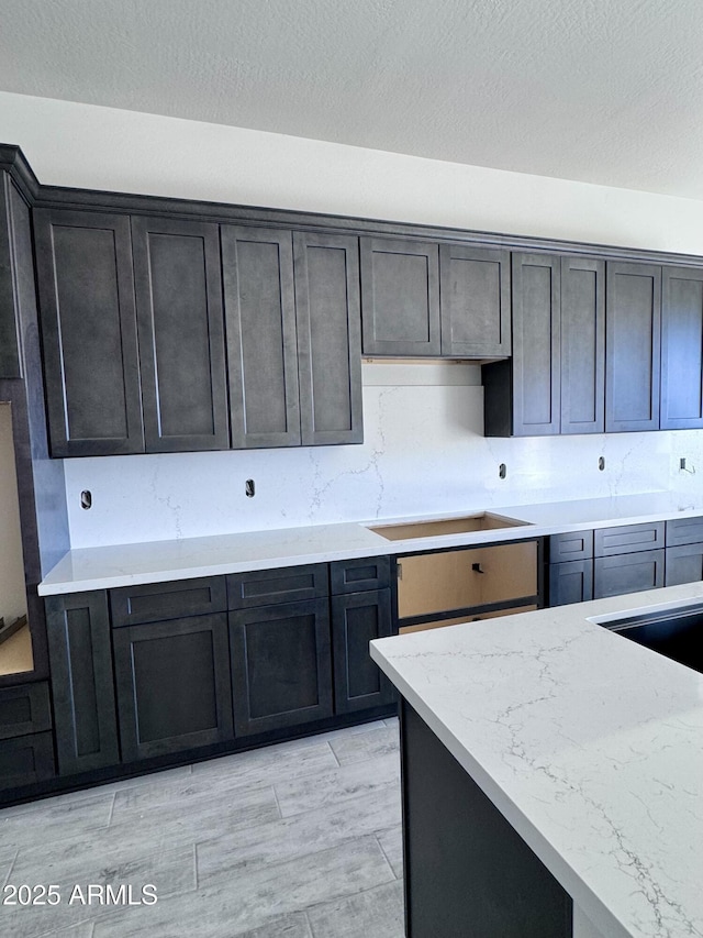 kitchen featuring a textured ceiling, light stone counters, light wood-style floors, backsplash, and cooktop