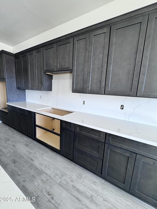 kitchen featuring tasteful backsplash, dark cabinetry, cooktop, and light wood-style floors