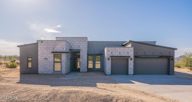 contemporary house with concrete driveway, stone siding, an attached garage, and stucco siding