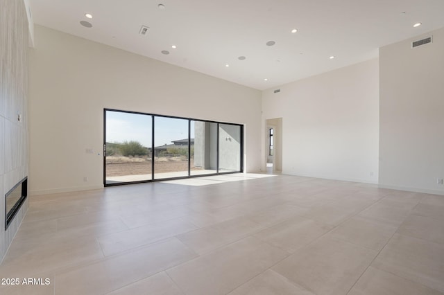 spare room featuring a large fireplace, a high ceiling, visible vents, and recessed lighting