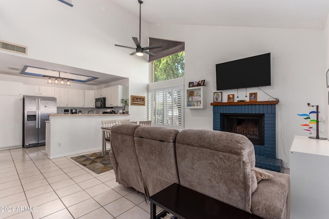 tiled living room with ceiling fan, high vaulted ceiling, and a brick fireplace