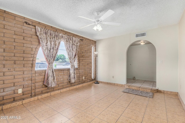 6430 W Thomas Rd, Phoenix, AZ 85033 - unfurnished room featuring a textured ceiling, tile patterned flooring, brick wall, arched walkways, and a ceiling fan