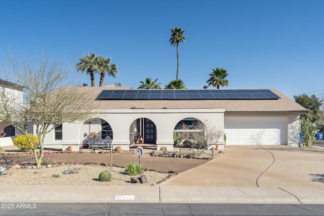 view of front of property with roof mounted solar panels, a garage, driveway, and stucco siding