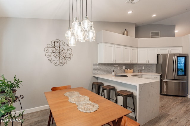 kitchen with light hardwood / wood-style floors, kitchen peninsula, white cabinetry, stainless steel refrigerator, and vaulted ceiling