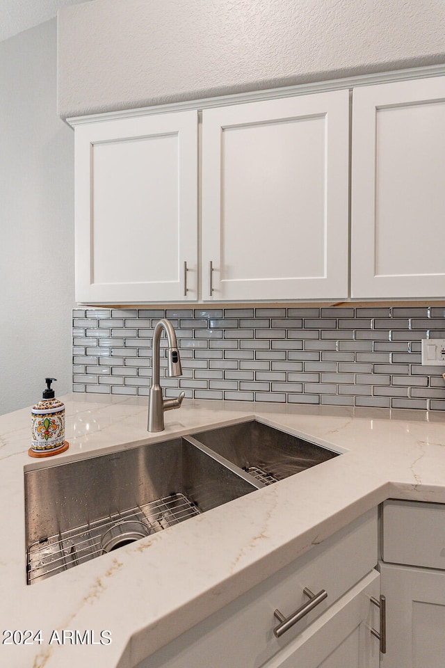 details featuring white cabinets, light stone countertops, backsplash, and sink