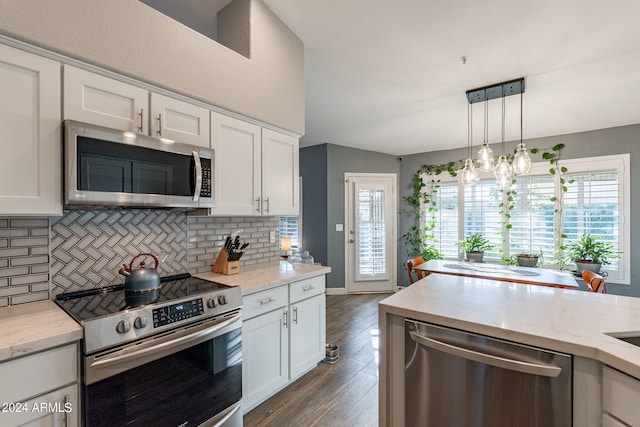 kitchen with light stone counters, white cabinets, decorative light fixtures, dark wood-type flooring, and appliances with stainless steel finishes