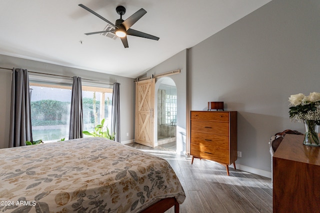 bedroom with lofted ceiling, ceiling fan, hardwood / wood-style flooring, ensuite bath, and a barn door