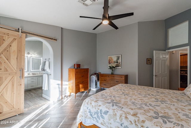 bedroom with ensuite bath, ceiling fan, a barn door, and hardwood / wood-style floors