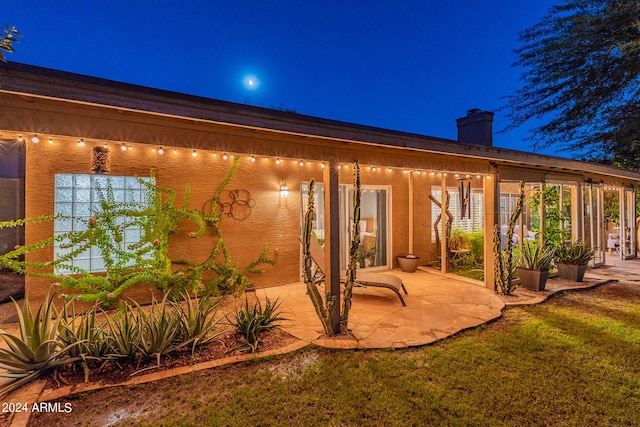 back house at night featuring a patio and a lawn