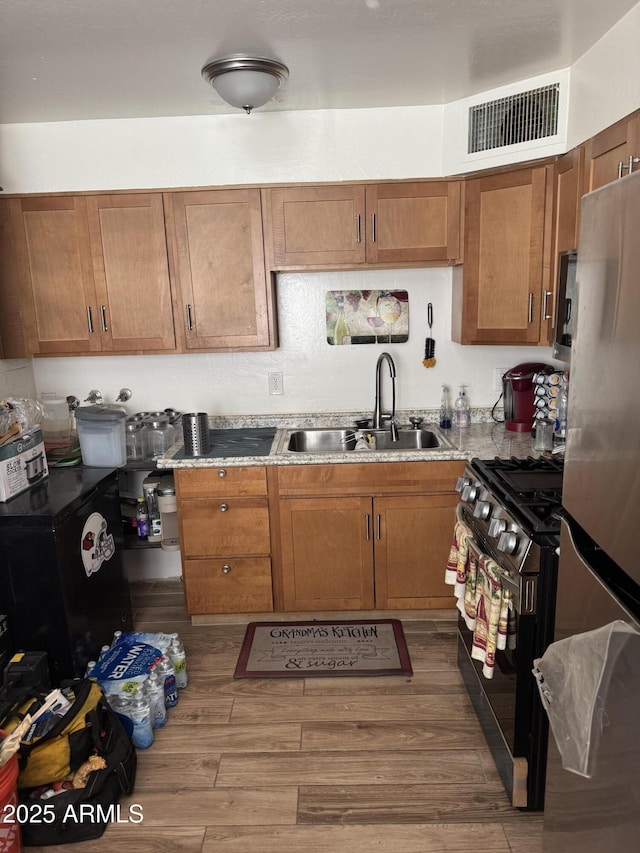 kitchen with sink, gas range, dark wood-type flooring, and stainless steel refrigerator