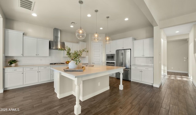 kitchen with wall chimney range hood, decorative backsplash, visible vents, appliances with stainless steel finishes, and white cabinets
