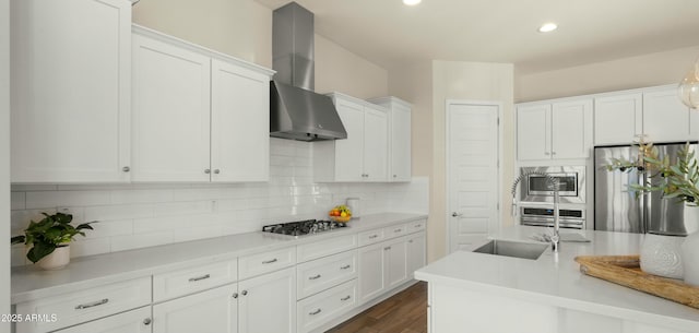 kitchen featuring wall chimney range hood, decorative backsplash, light countertops, stainless steel appliances, and white cabinetry