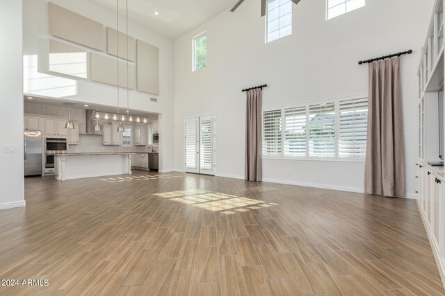 unfurnished living room featuring a wealth of natural light, a towering ceiling, and hardwood / wood-style flooring