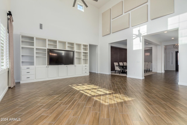 unfurnished living room featuring a towering ceiling, ceiling fan, dark wood-type flooring, and plenty of natural light