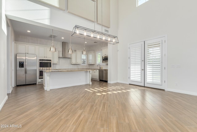 kitchen with a center island, wall chimney exhaust hood, appliances with stainless steel finishes, a healthy amount of sunlight, and decorative light fixtures