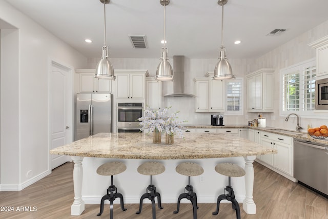 kitchen with appliances with stainless steel finishes, a kitchen island, hanging light fixtures, and wall chimney range hood