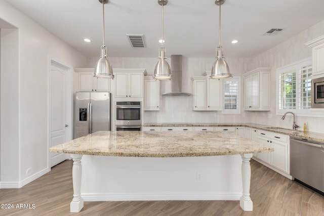 kitchen featuring a kitchen island, pendant lighting, stainless steel appliances, sink, and wall chimney range hood