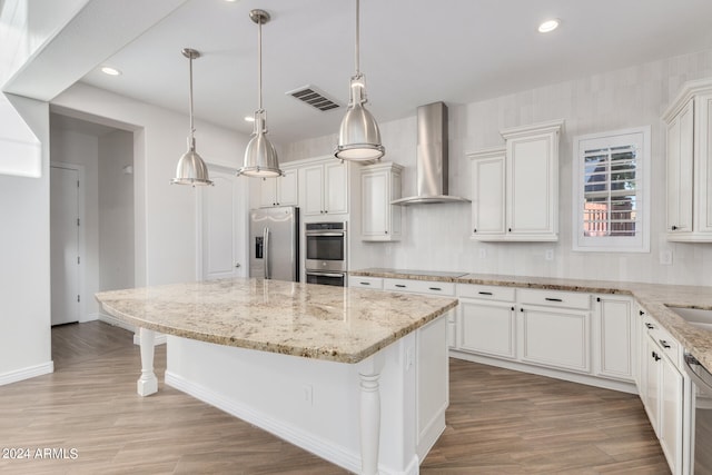 kitchen featuring wall chimney exhaust hood, white cabinets, appliances with stainless steel finishes, and pendant lighting