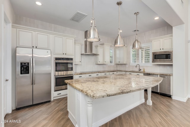 kitchen with hanging light fixtures, white cabinetry, stainless steel appliances, a center island, and light hardwood / wood-style flooring