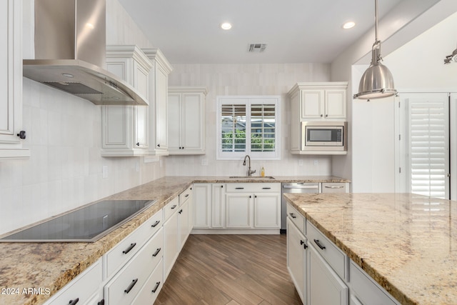 kitchen featuring pendant lighting, sink, white cabinets, wall chimney range hood, and appliances with stainless steel finishes