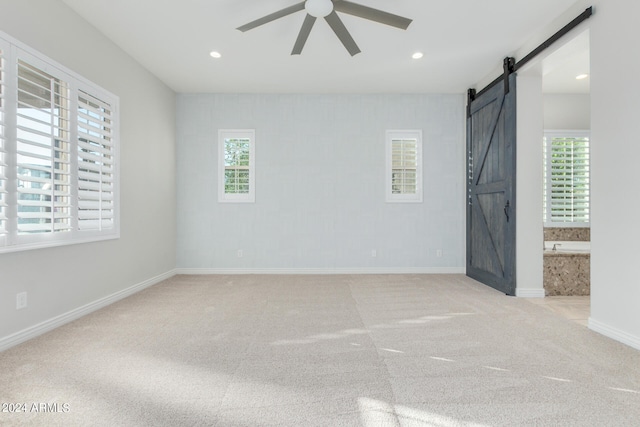 carpeted spare room featuring a barn door and ceiling fan