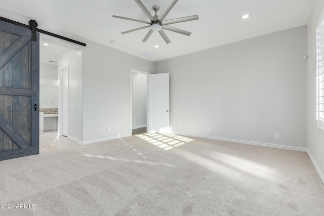 unfurnished bedroom with light carpet, connected bathroom, ceiling fan, and a barn door