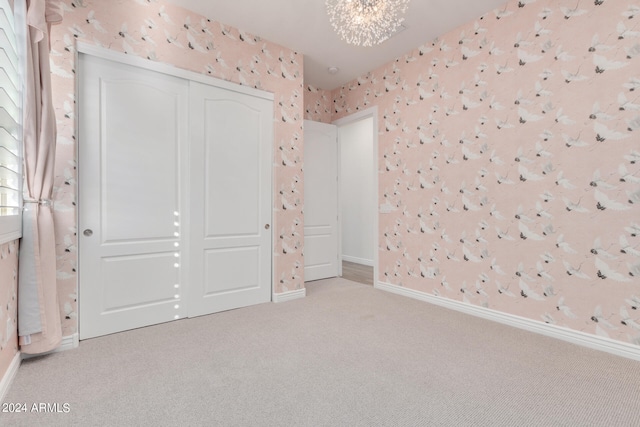 unfurnished bedroom with a closet, light colored carpet, and a notable chandelier