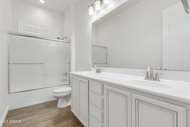 full bathroom featuring wood-type flooring, combined bath / shower with glass door, vanity, and toilet