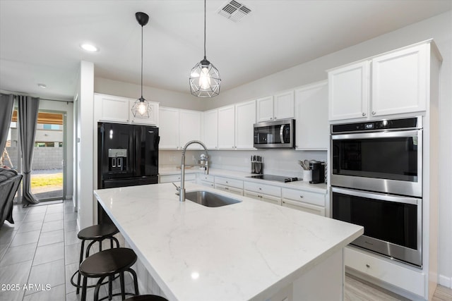 kitchen with sink, a kitchen island with sink, white cabinetry, light stone counters, and black appliances