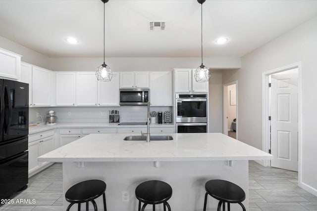 kitchen featuring stainless steel appliances, an island with sink, pendant lighting, and white cabinets